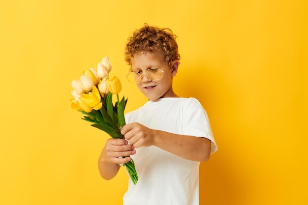 子供の頃の楽しみをポーズする黄色い花を持つ写真の肖像画の巻き毛の小さな男の子は、変更されていない背景を分離しました