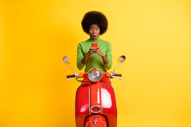 鮮やかな黄色の背景で隔離のカジュアルな緑のジャンパーを身に着けている両手で携帯電話を保持しているオートバイの興奮したバイカーライダードライバーの写真の肖像画