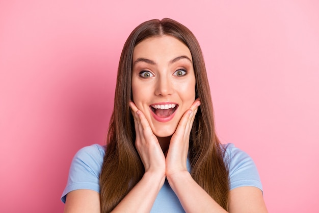 Photo portrait of excited girl touching face with two hands with open mouth isolated on pastel pink colored background