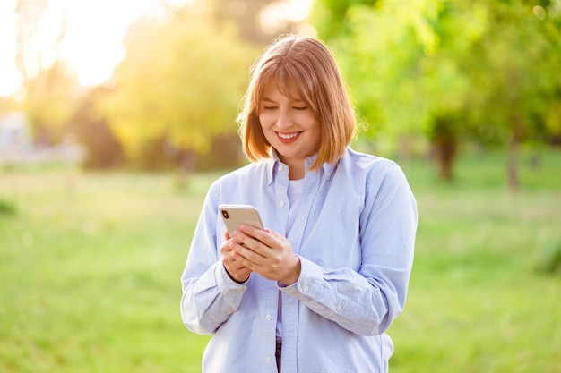 Photo portrait female student in blue shirt keeping cellphone browsing internet walking along park