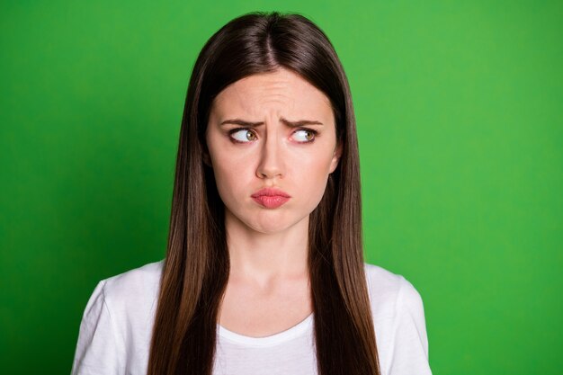 Foto ritratto di ragazza triste accigliata che guarda al lato isolato su sfondo colorato verde vivido