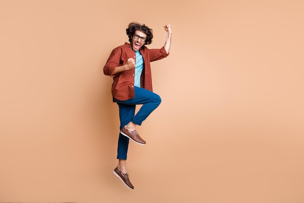 Photo portrait full body view of excited guy celebrating isolated on pastel beige colored background