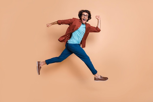 파스텔 베이지 색 배경에 고립 된 점프 실행 웃는 남자의 사진 초상화 전신보기