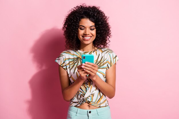 Foto ritratto di ragazza che tiene il telefono in due mani isolato su sfondo colorato rosa pastello