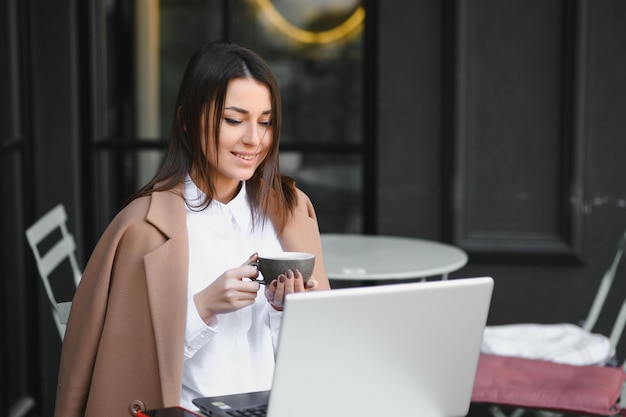 コーヒーを飲みながらカフェに座ってラップトップタイピングに取り組んでいるゴージャスな魅力的な女性の写真の肖像画