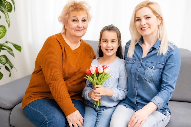 Photo portrait of granddaughter congratulating granny giving tulips bunch sitting near mom.