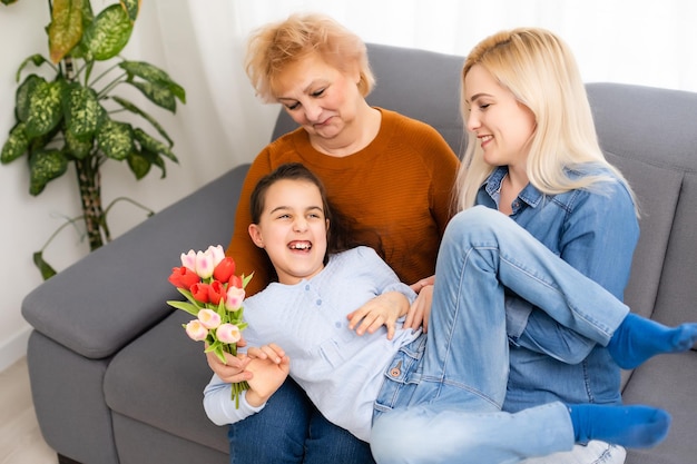 Photo portrait of granddaughter congratulating granny giving tulips bunch sitting near mom.