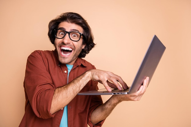 Foto ritratto fotografico di un hacker pazzo che digita tenendo in mano il laptop isolato su sfondo colorato beige pastello