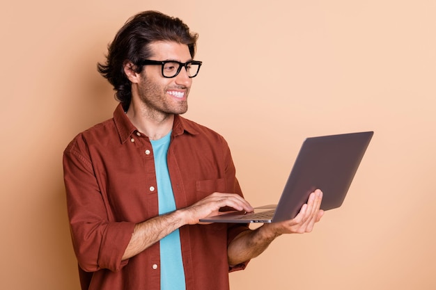 Photo portrait of man holding laptop in hand typing isolated on pastel beige colored background