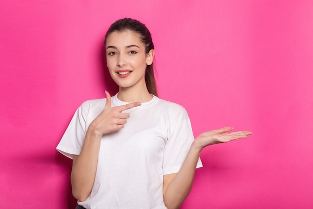 Photo portrait of schoolgirl pointing finger at your product blank space holding hand palm wearing top checkered shirt isolated on pink colored background