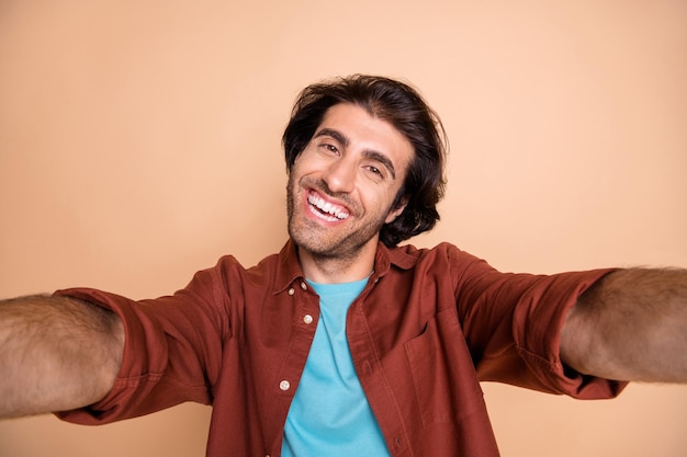 Photo portrait of smiling man taking selfie isolated on pastel beige colored background