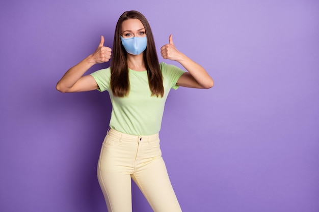 Photo portrait of woman giving two thumbs up wear medical mask isolated on vivid violet colored background