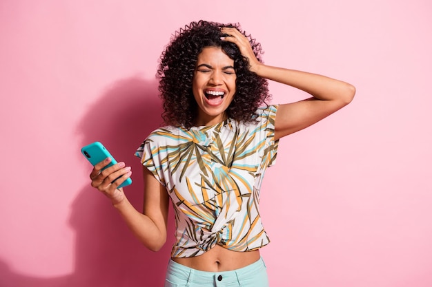 파스텔 핑크색 배경에 격리된 전화를 들고 웃고 있는 한 손으로 머리를 잡고 있는 여성의 사진 초상화
