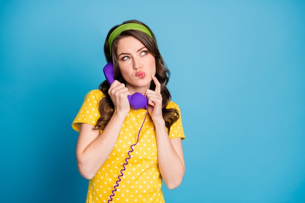 파스텔 연한 파란색 배경에 격리된 보라색 전화를 들고 손가락으로 얼굴을 만지는 여성의 사진 초상화