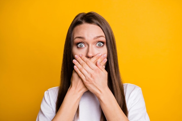 Photo portrait of young afraid girl shut mouth with hands staring worried isolated on vibrant yellow color background