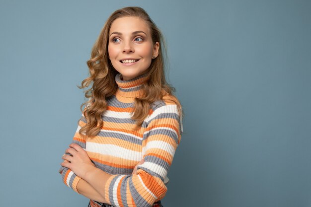 Photo portrait of young beautiful nice positive smiling blonde woman wearing striped pullover isolated over blue background with copy space.