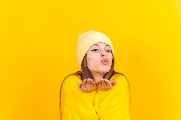 Photo portrait of a young woman blowing a kiss isolated on a yellow background woolen sweater