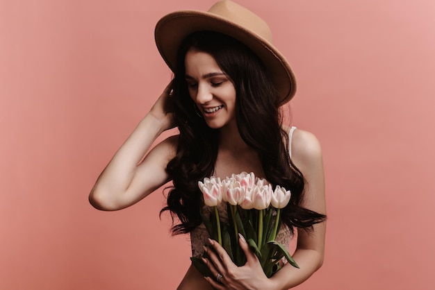 Photo portrait of a young woman smiling holding a bouquet of tulips isolated against a pastel pink