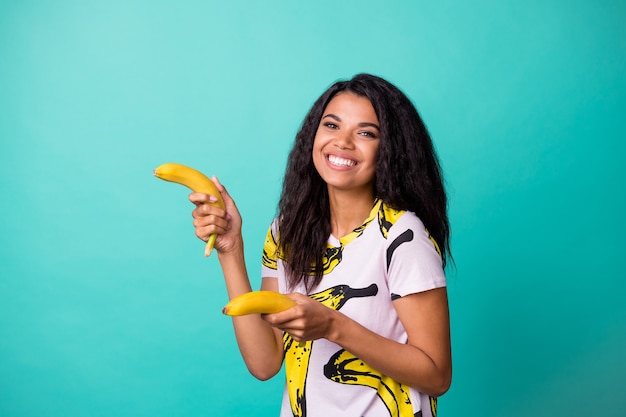 Photo of positive afro american girl hold two bananas isolated over turquoise color background