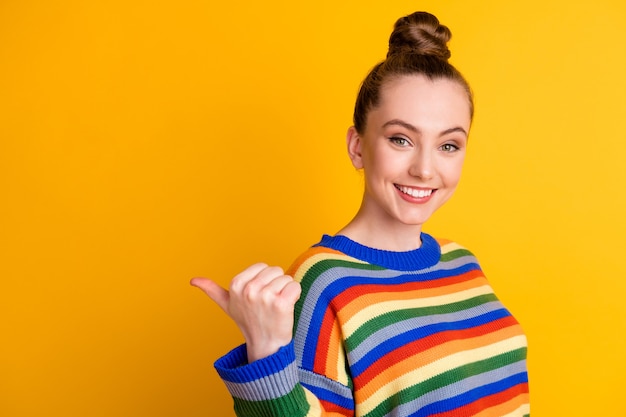 Photo of positive cheerful girl point thumb finger copyspace choose decide advise adverts promo wear good look pullover isolated over bright color background