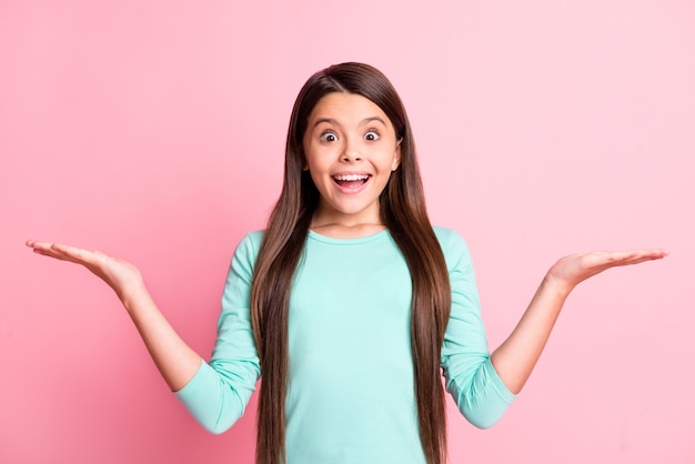 ポジティブかわいいかわいいラテン女性の長い髪型の写真は手を上げて空のスペースを保持します提案を示しています興奮した笑顔はターコイズのスウェットシャツを着用します孤立したピンク色の背景