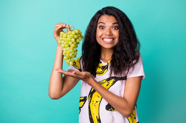 Photo of positive dark skin girl present viticulture eco grapevine wear pink t-shirt isolated over teal color background