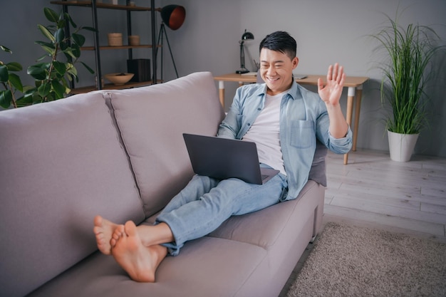 Photo of positive funny japanese man sit couch enjoy distance conference wear casual shirt in home indoors