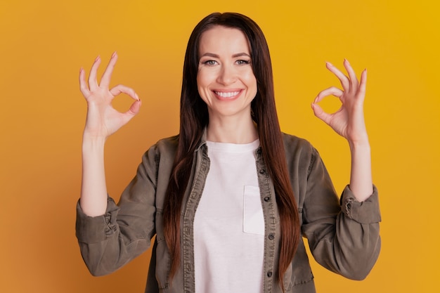 Photo of positive girl show ok-sign ad isolated over yellow background