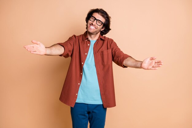 Photo of positive guy open arms want hug you toothy smile wear eyewear brown t-shirt isolated beige color background