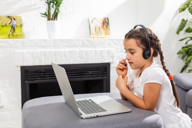 Foto di una ragazzina positiva che studia a distanza il tavolo della scrivania usa il laptop ha una lezione di comunicazione online con il tutor che scrive un rapporto in casa al chiuso