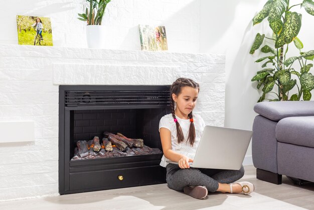 Фотография положительного ребенка, изучающего ноутбук удаленного использования, имеет урок онлайн-общения с репетитором, пишущим отчет в доме, в помещении
