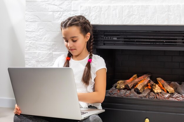 Photo of positive kid girl study remote use laptop have online communication lesson with tutor writing report in house indoors