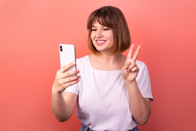 Photo positive lady make selfie fingers show vsign have good mood isolated on pink background