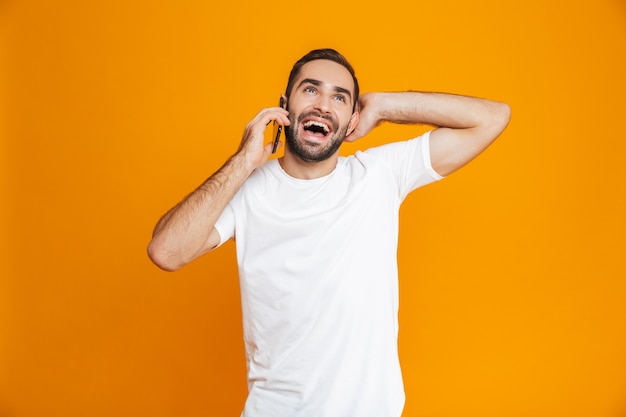 Photo of positive man 30s in casual wear smiling and talking on mobile phone, isolated