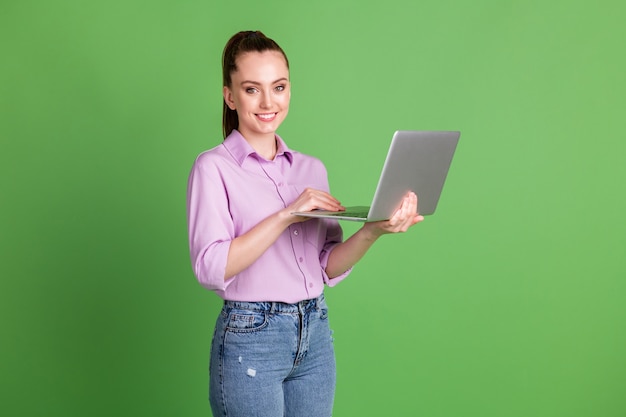 Photo of positive manager girl work remote laptop texting typing enjoy social networking communication wifi connection wear lilac denim jeans isolated over green color background