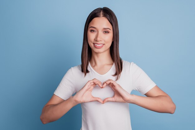 Photo of positive romantic girlfriend fingers show heart gesture on blue background