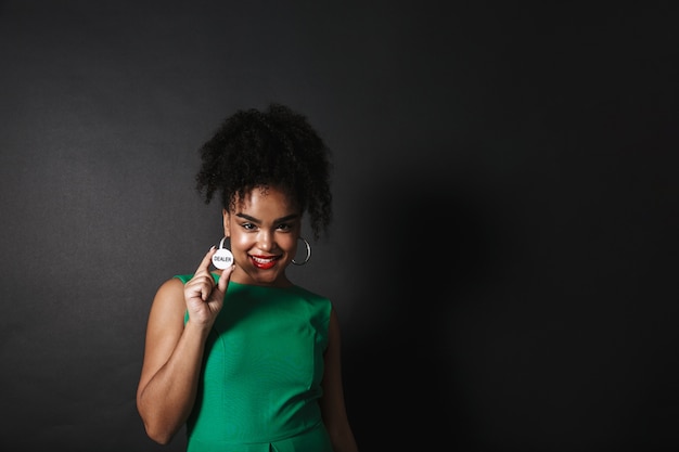 Photo of pretty afro american woman wearing green dress showing casino token