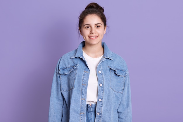 Photo of pretty cheerful gorgeous woman, brunette girl wearing white shirt and denim jacket posing isolated over lilac wall