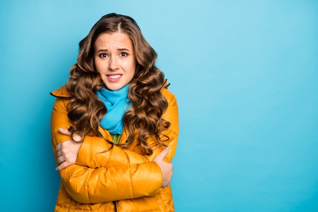 Photo of pretty curly traveler lady upset frosty winter day shaking all body walk street hug herself wear trendy casual yellow overcoat blue scarf isolated blue color wall