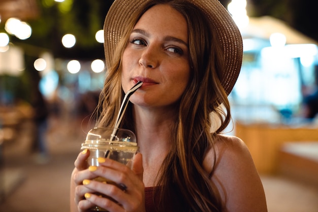 Photo of a pretty cute beautiful woman walking by street outdoors drinking juice at the evening night.