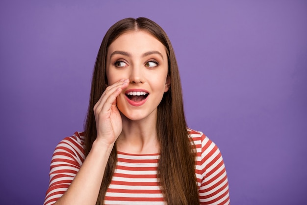 Photo of pretty funny curious lady look side empty space hand near mouth say tell news gossips people crowd wear casual striped shirt isolated pastel purple color wall