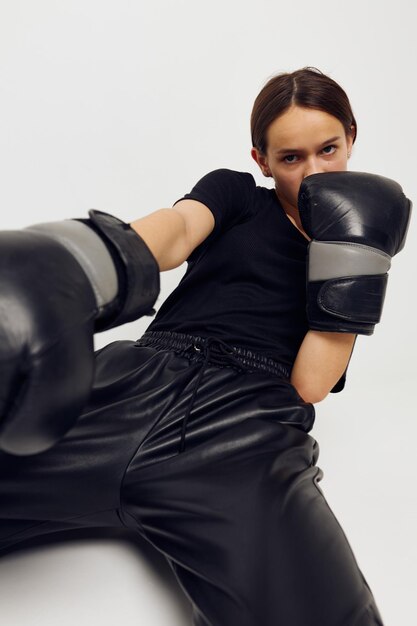 Фото красивой девушки в боксерских перчатках на полу в черной футболке на светлом фоне