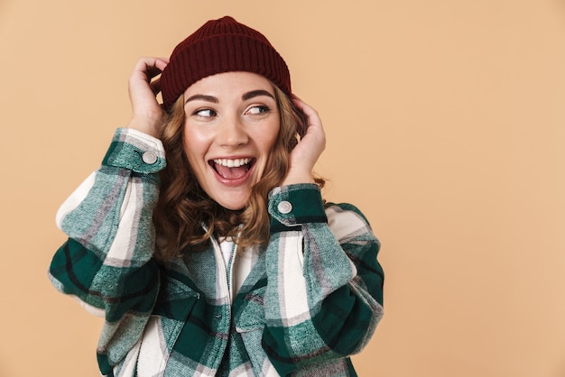 Foto di una donna abbastanza felice con un cappello lavorato a maglia in posa e sorridente isolato su beige