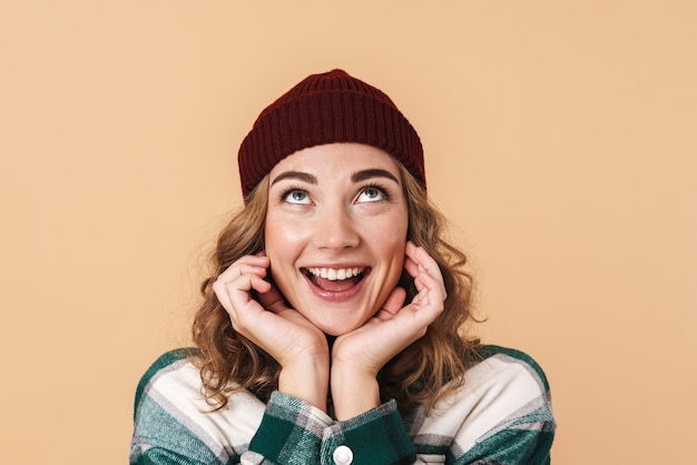 Photo of pretty happy woman in knit hat posing and smiling isolated on beige