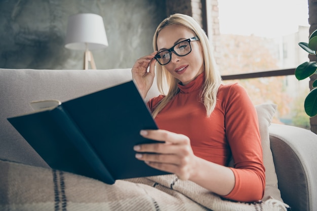 Photo of pretty homey lady holding favorite book novel in hands enjoy Saturday morning free time lying comfy couch covered blanket wear specs casual outfit flat indoors