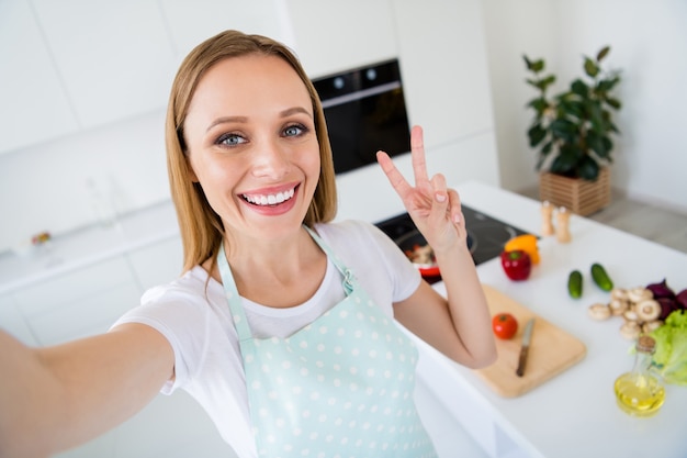 Photo of pretty housewife weekend morning cooking showing v-sign making selfies presenting followers traditional family recipe meal white kitchen indoors