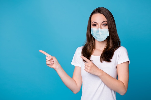 Photo of pretty lady sales trade manager direct fingers side up empty space show demonstrate covid quarantine novelty wear casual white t-shirt medical mask isolated blue color background