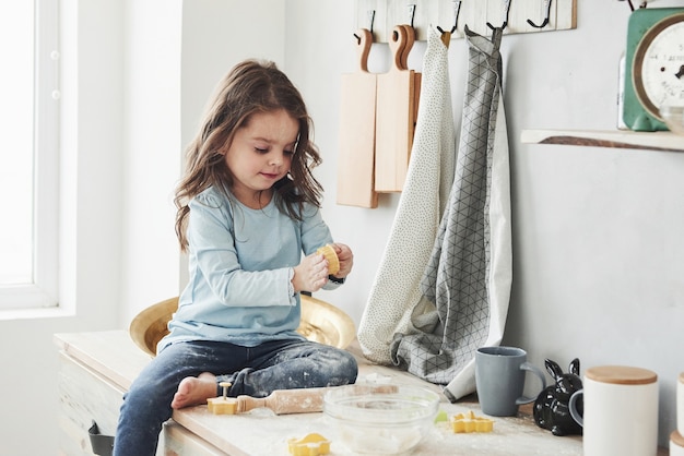 Photo of pretty little girl that sits on the kitchen table and plays with flour.