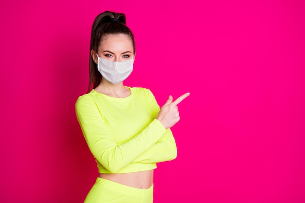 Foto di una bella ragazza carina punto spazio vuoto vestito sportivo maschera medica superiore isolato sfondo di colore rosa