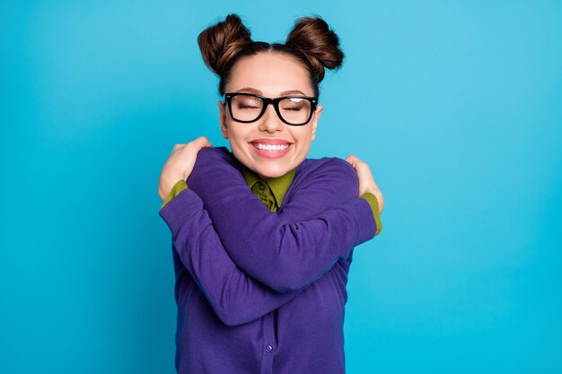 Foto di una studentessa piuttosto felice, due panini gli occhi chiusi, che si abbraccia la motivazione prima dell'esame del test, indossare le specifiche, il colletto della camicia, il maglione viola, lo sfondo di colore blu, isolato